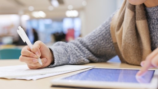 Student working on a tablet and writing on a notepad